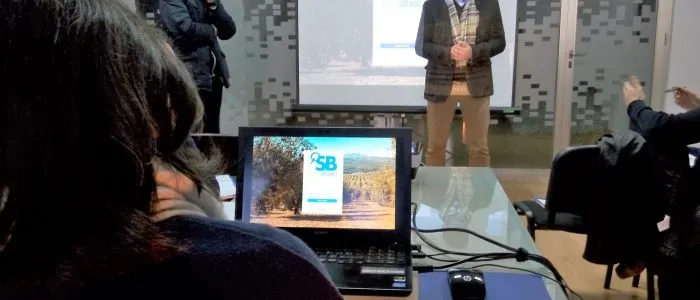 Portátil de un asistente que muestra el acceso a la plataforma de SB, con un ponente de pie al fondo