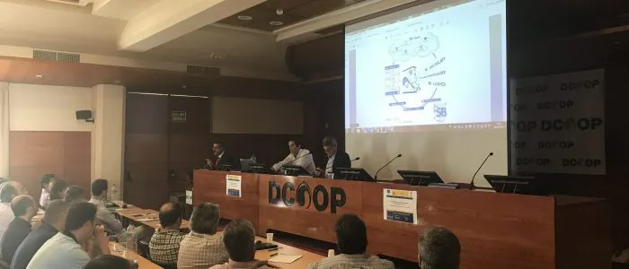 Tres ponentes en la mesa de Dcoop ante una diapositiva con el esquema circular de la solución web de SB para auditorías