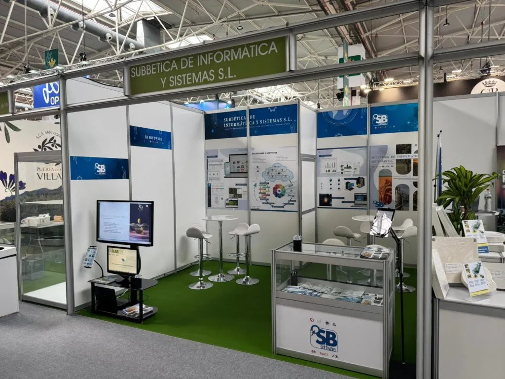 El stand de Subbética de Informática y Sistemas visto desde el pasillo, con pantallas, mesas altas y vitrina