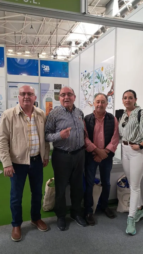 Tres hombres y una mujer posan a la entrada del stand, con el panel del olivo de SB Almazara al fondo