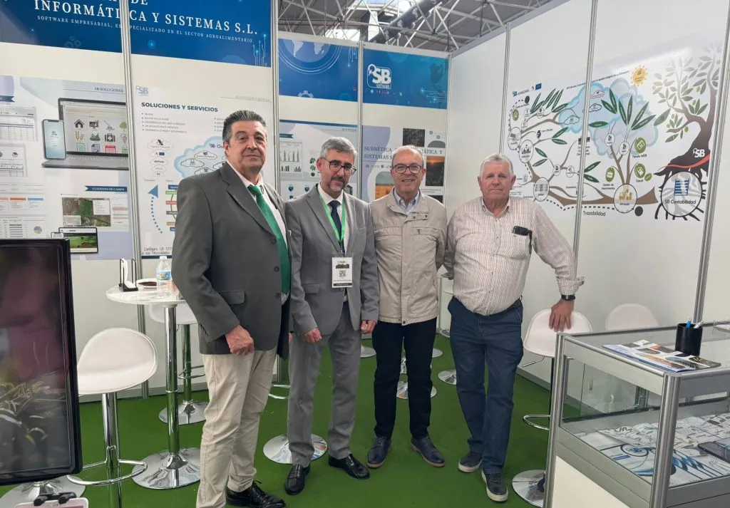 Cuatro hombres posan en el stand, delante de los paneles de soluciones y servicios y del olivo de SB Almazara