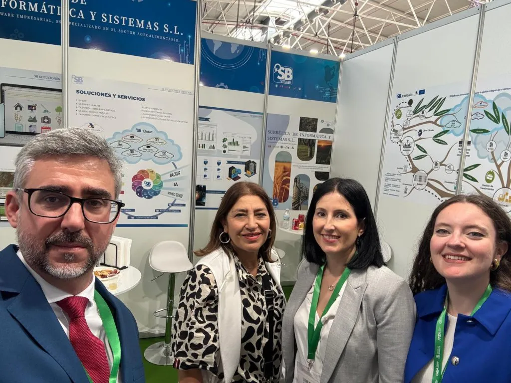 Un hombre y tres mujeres se hacen un selfi en el stand, ante los paneles de soluciones y servicios y de SB Almazara
