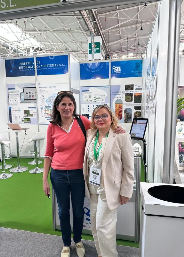 Dos mujeres posan abrazadas en la entrada del stand, ante los paneles de Subbética de Informática y Sistemas