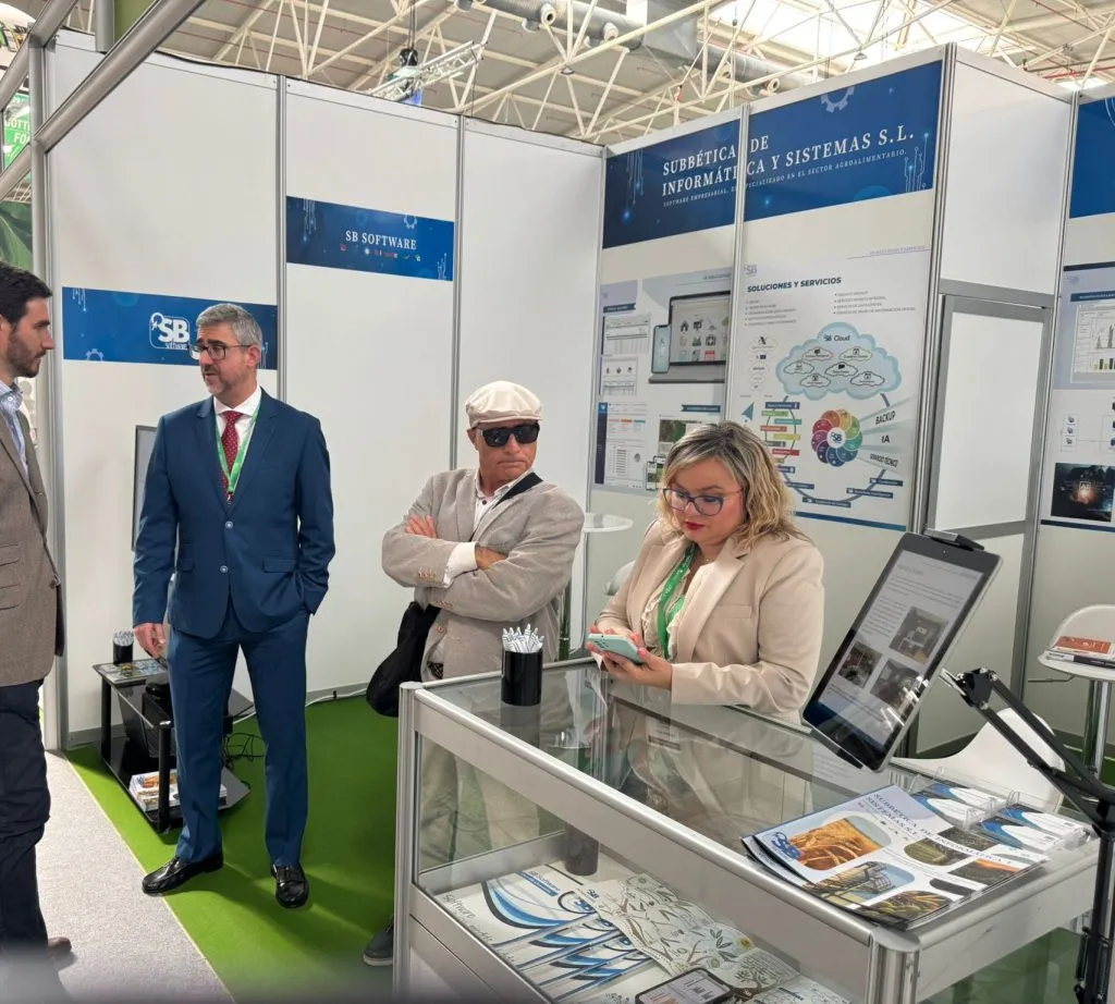 Visitantes en el stand de SB Software, junto a la vitrina con folletos y una tableta en su soporte