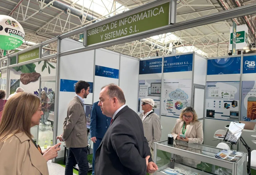 Visitantes conversan en el pasillo frente al stand de Subbética de Informática y Sistemas, bajo su rótulo verde